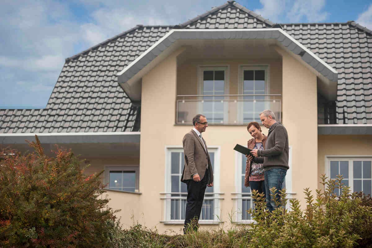 Three people in front of a modern house review documents, showing decision-making.