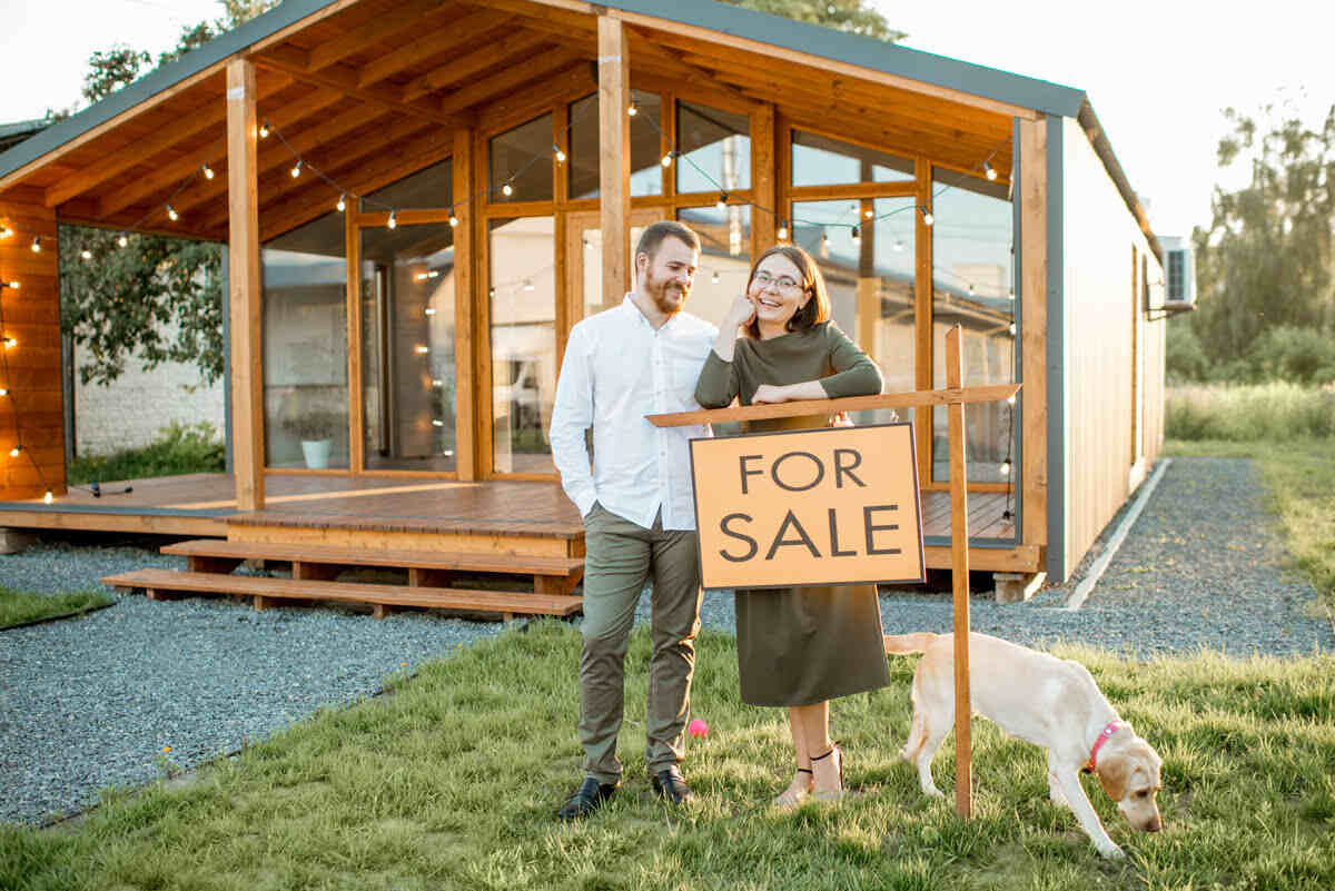 Couple smiling and standing behind house sale sign