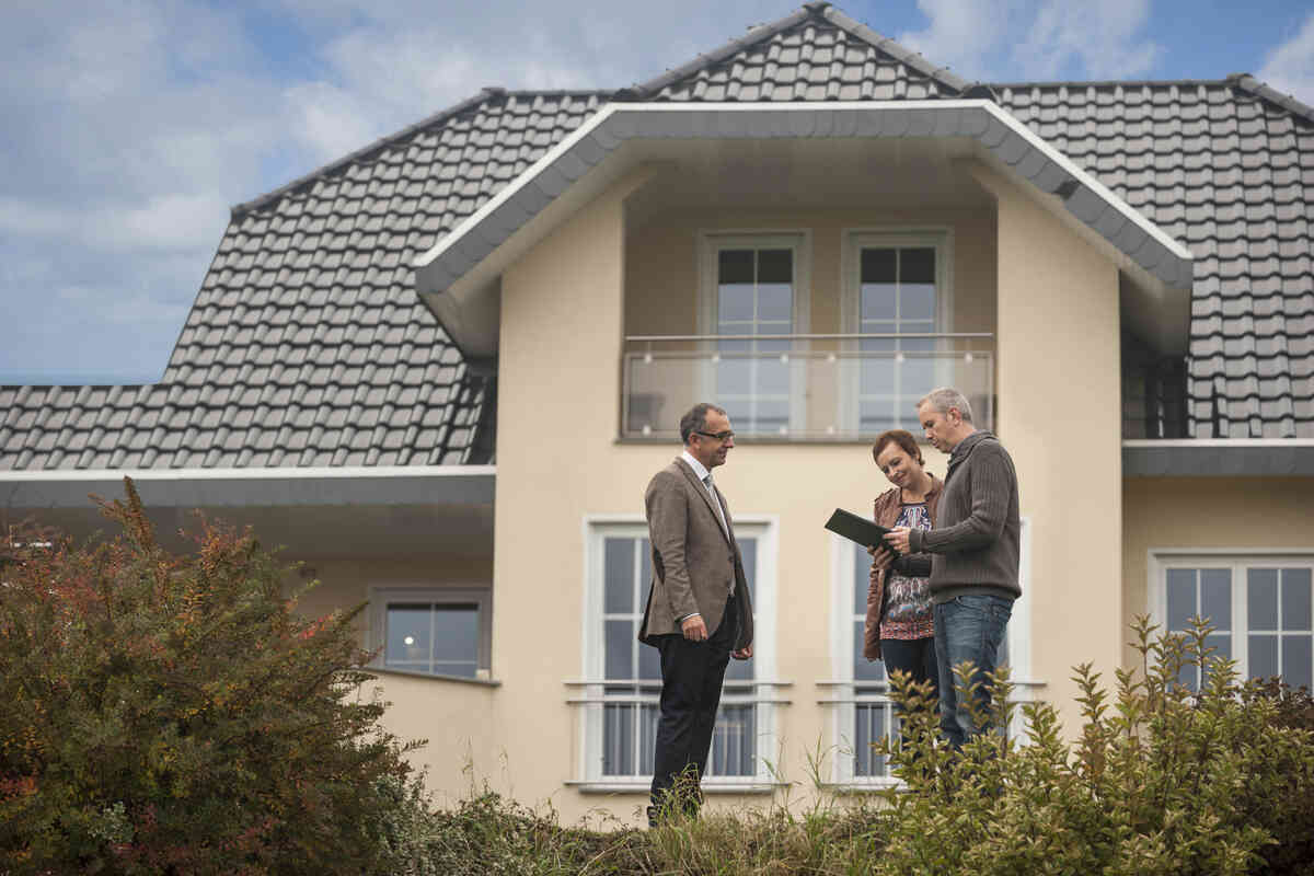 Three people in front of a modern house review documents, showing decision-making.