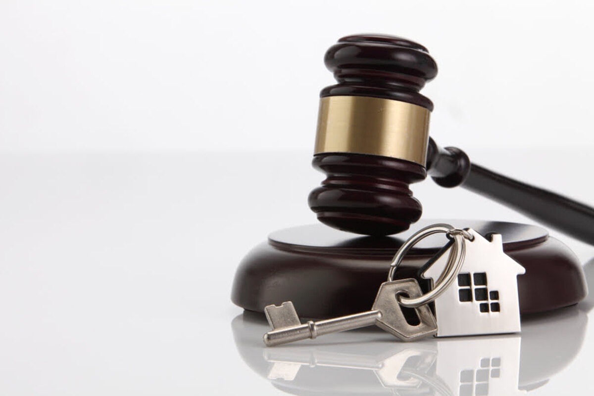 a wooden judge's gavel next to a house key with a house pendant