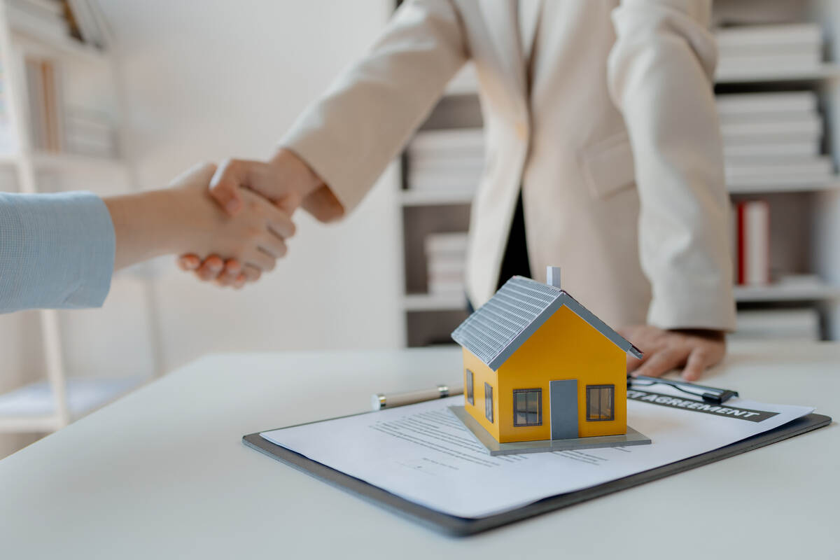 Handshake over contract with yellow house model on table, symbolizing a successful real estate deal.