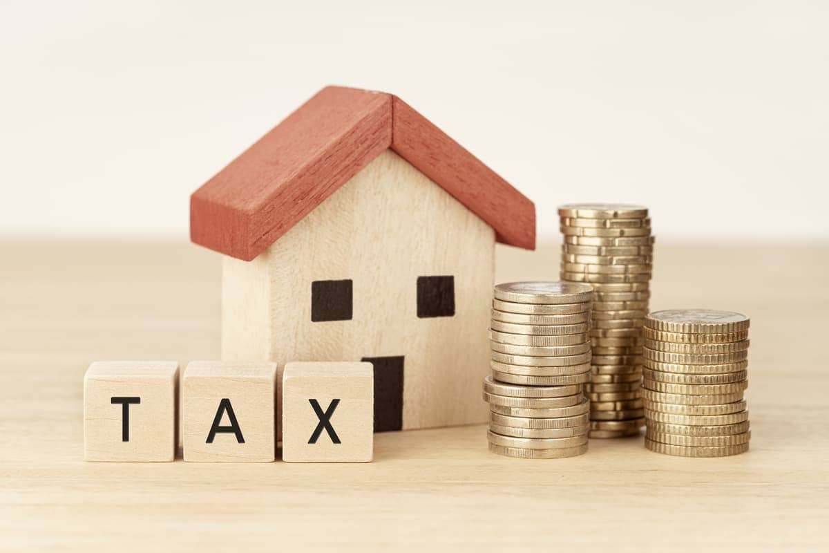 Model of a house with a tax sign and coins in front of it