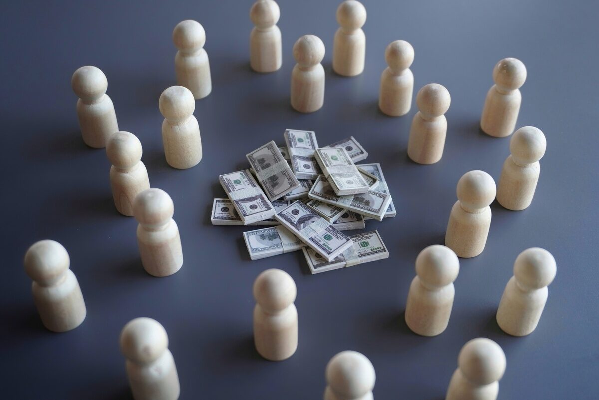 Wooden figures surround dollar stacks on gray, symbolizing finance, teamwork, and investment.