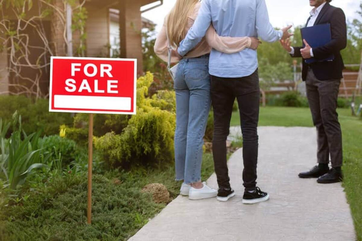 A man and a woman are talking to a real estate agent in front of a house and a for sale sign
