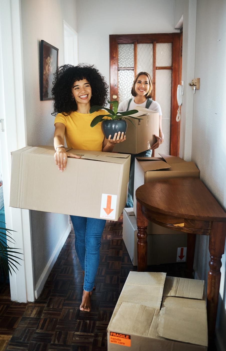 Two people carrying moving boxes into a new home